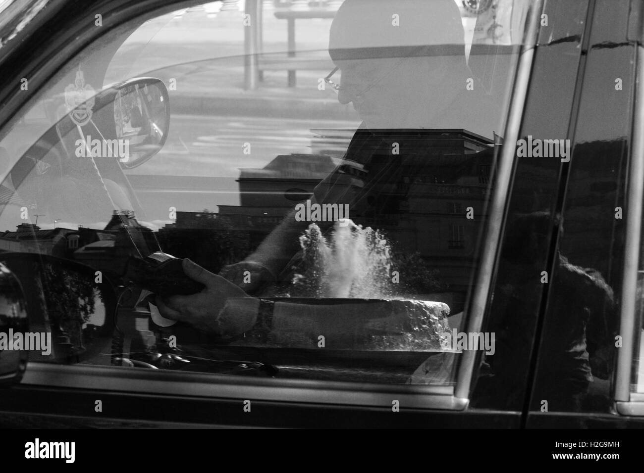 Un chauffeur de taxi de Londres prendre un paiement par carte à Trafalgar Square - un reflet de l'une des fontaines de la porte fenêtre. Banque D'Images