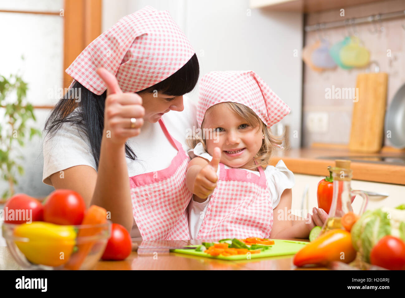 Heureuse mère et fille avec des légumes frais showing Thumbs up geste. Tourné dans la cuisine Banque D'Images