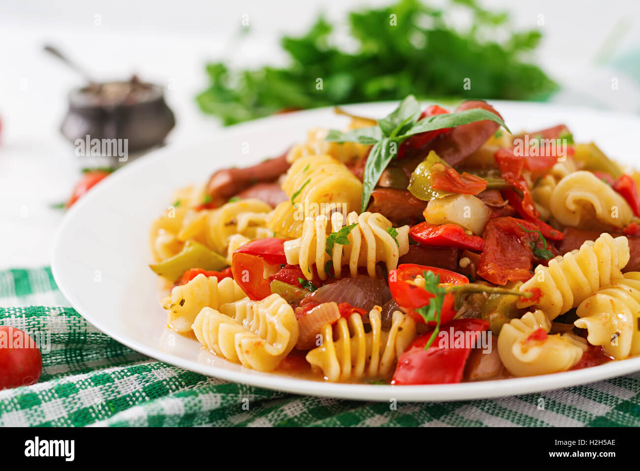 Les pâtes à la sauce tomate avec des saucisses, tomates, basilic vert décoré en plaque blanche sur un fond de bois. Banque D'Images