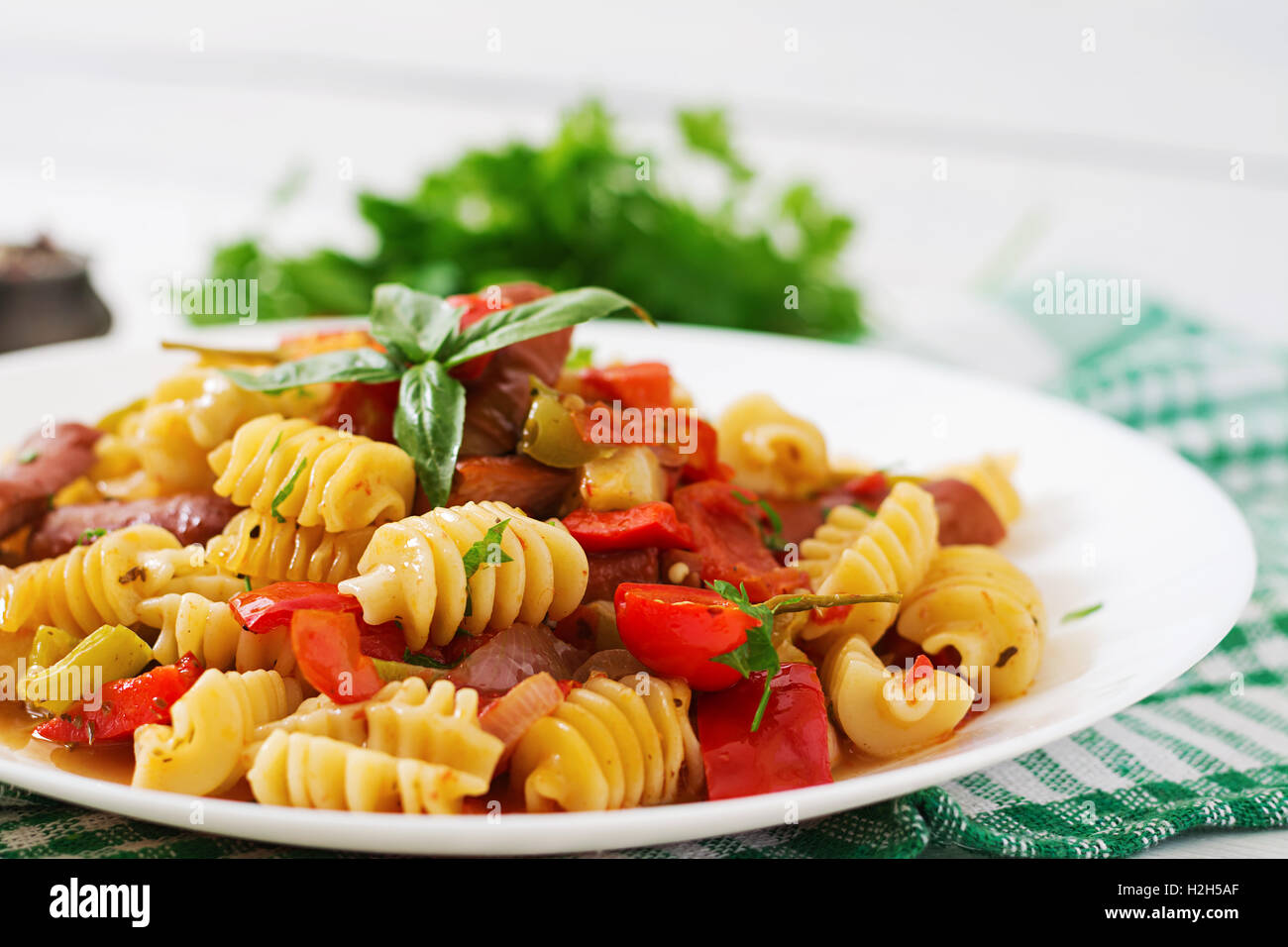 Les pâtes à la sauce tomate avec des saucisses, tomates, basilic vert décoré en plaque blanche sur un fond de bois. Banque D'Images
