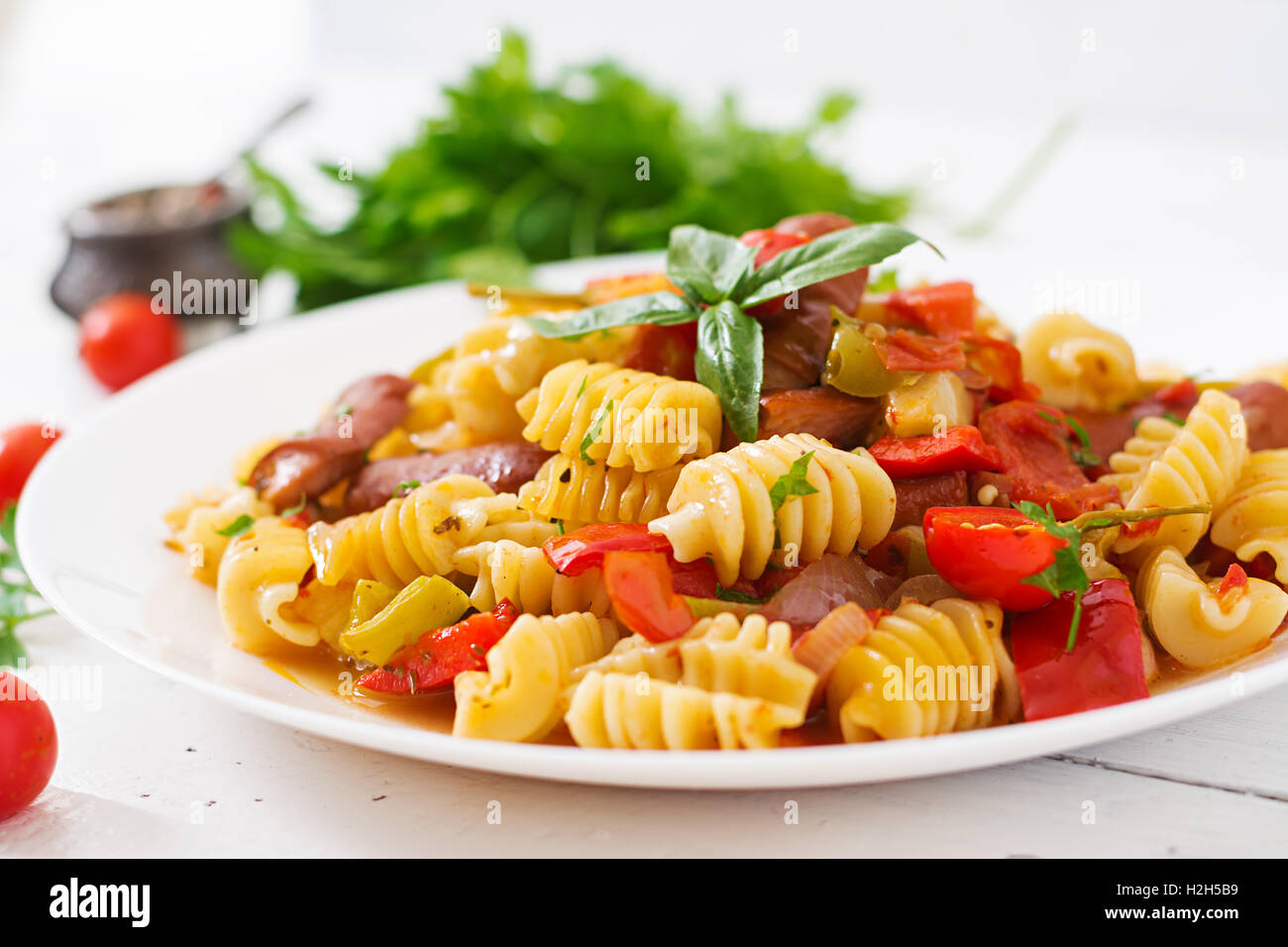 Les pâtes à la sauce tomate avec des saucisses, tomates, basilic vert décoré en plaque blanche sur un fond de bois. Banque D'Images