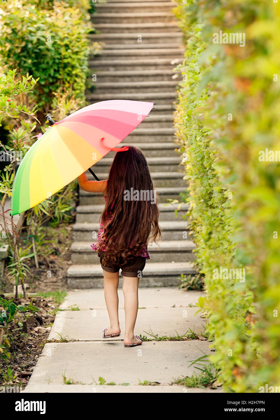 Vue arrière de petite fille portant parapluie arc-en-ciel Banque D'Images