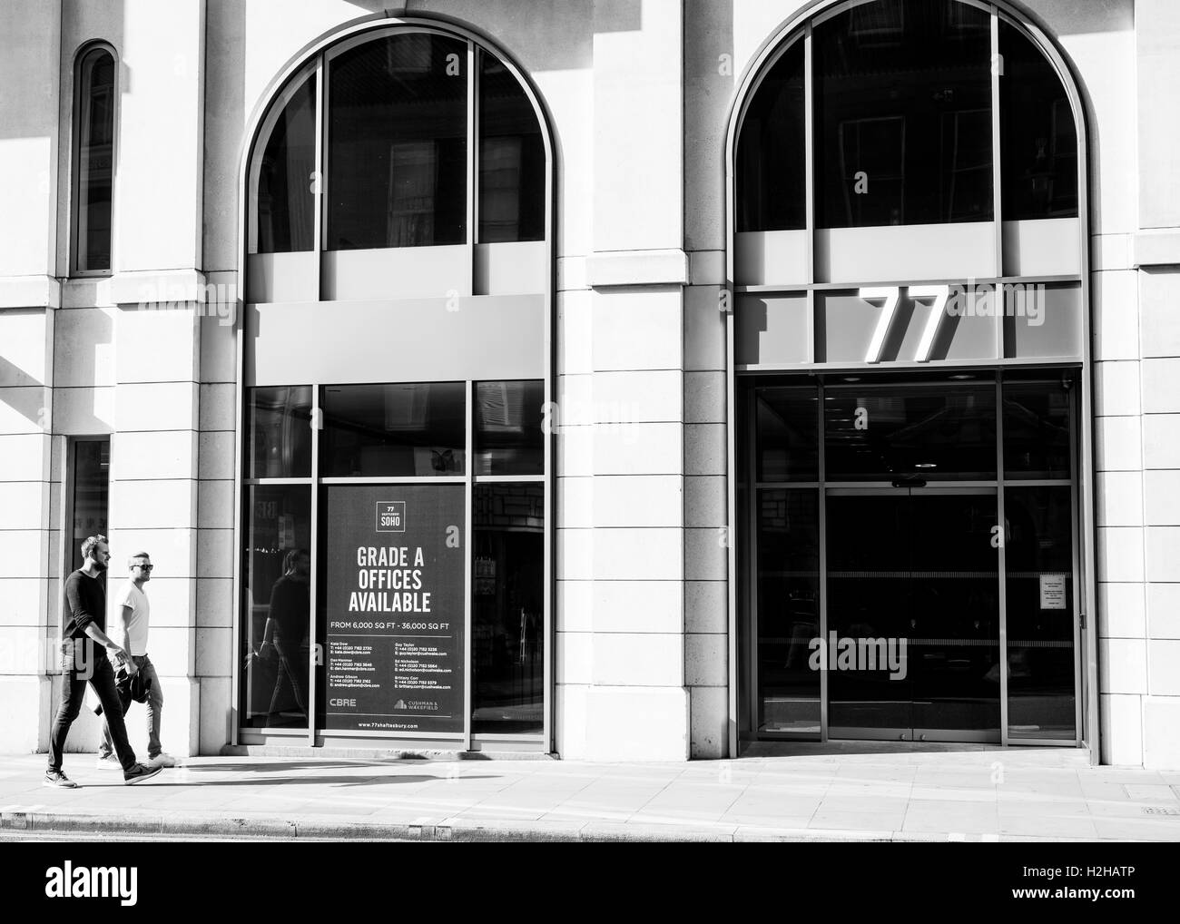 Deux jeunes hommes marchant sur le trottoir en face d'un bâtiment avec de grandes fenêtres et de panneaux la promotion de grade A offices Banque D'Images