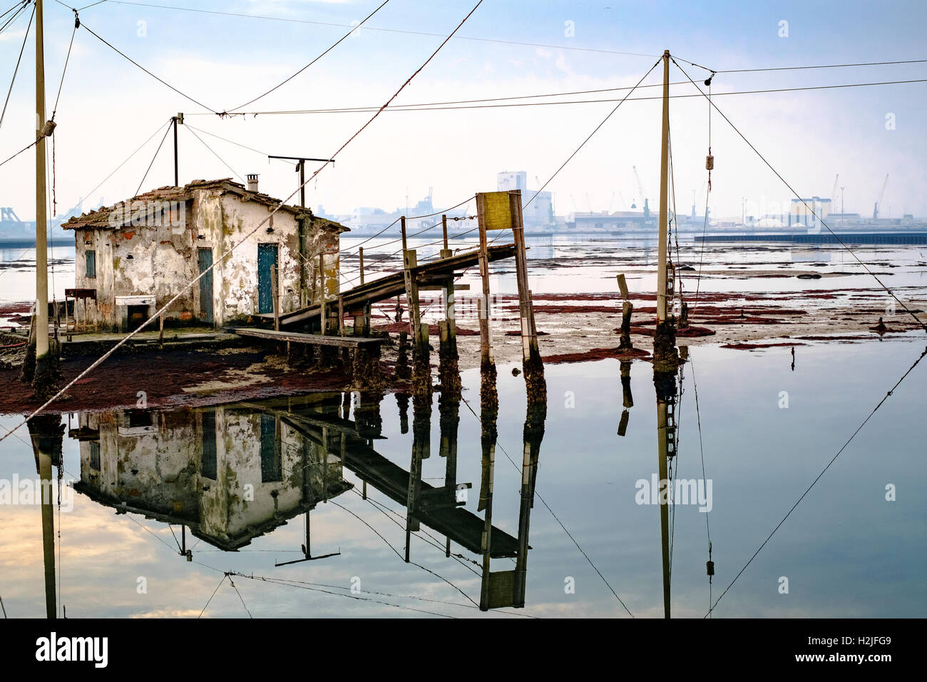 Ancienne maison de pêcheurs se reflétant dans la lagune de Marina di Ravenna, port industriel sur l'arrière-plan. Banque D'Images