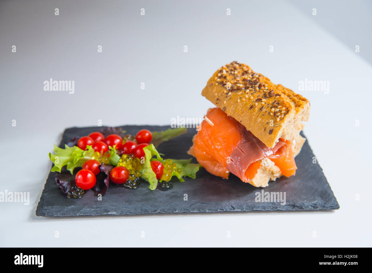 Saumon fumé sandwich complet, avec salade composée de laitue, tomates cerises et perles d'huile d'olive. Banque D'Images