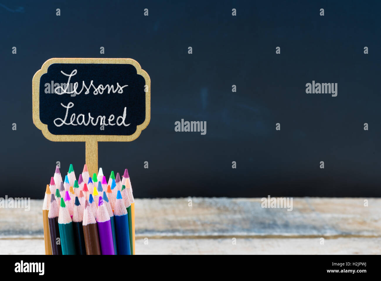 Mini tableau noir en bois avec label message Leçons tirées et crayons de couleur sur l'arrière-plan du tableau, copie de l'espace disponible, de l'éducation concept Banque D'Images