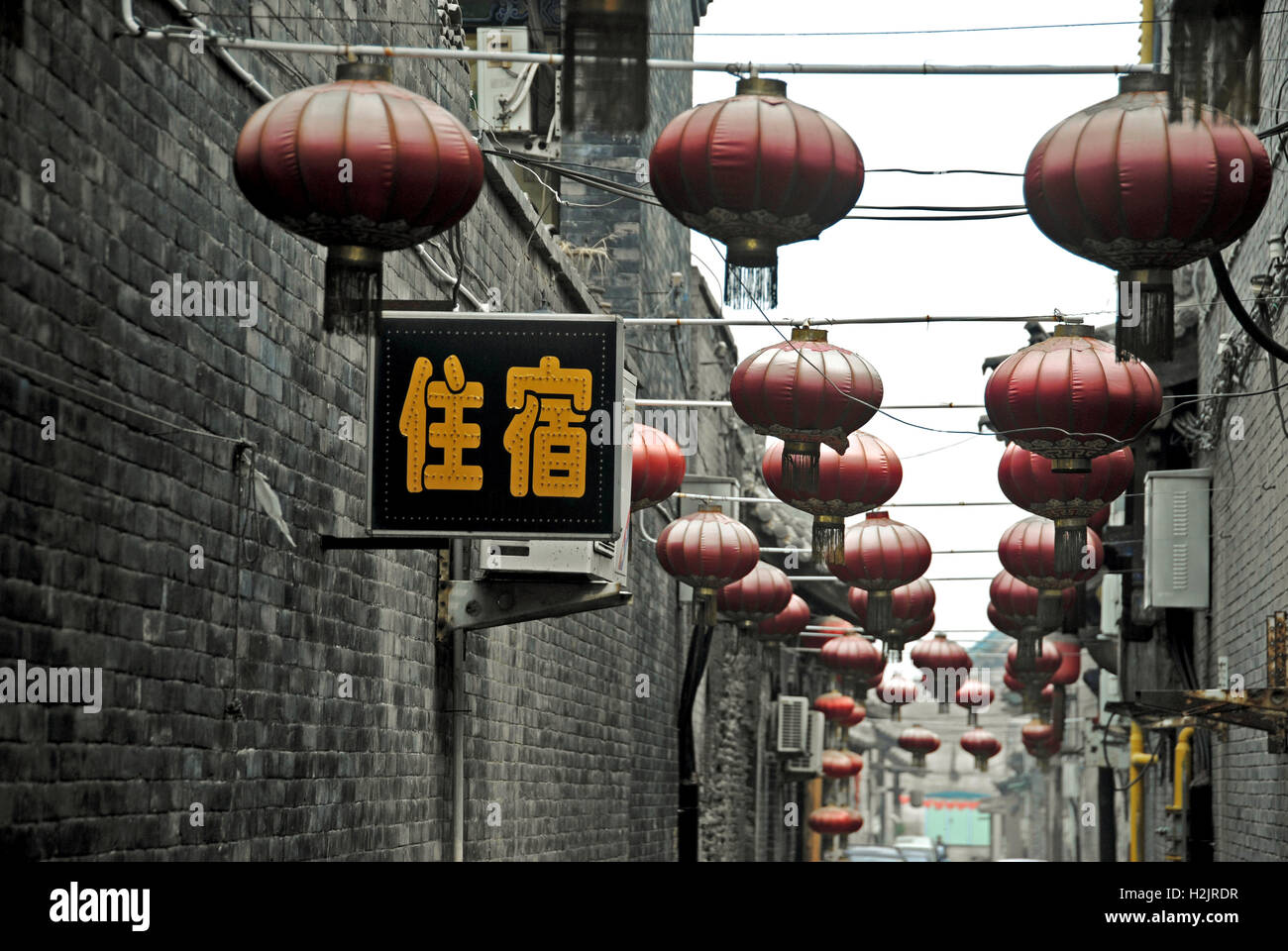 Un signe d'adaptation chinois accrochés entre les lanternes rouges dans une rue arrière à Pingyao, Chine. Banque D'Images