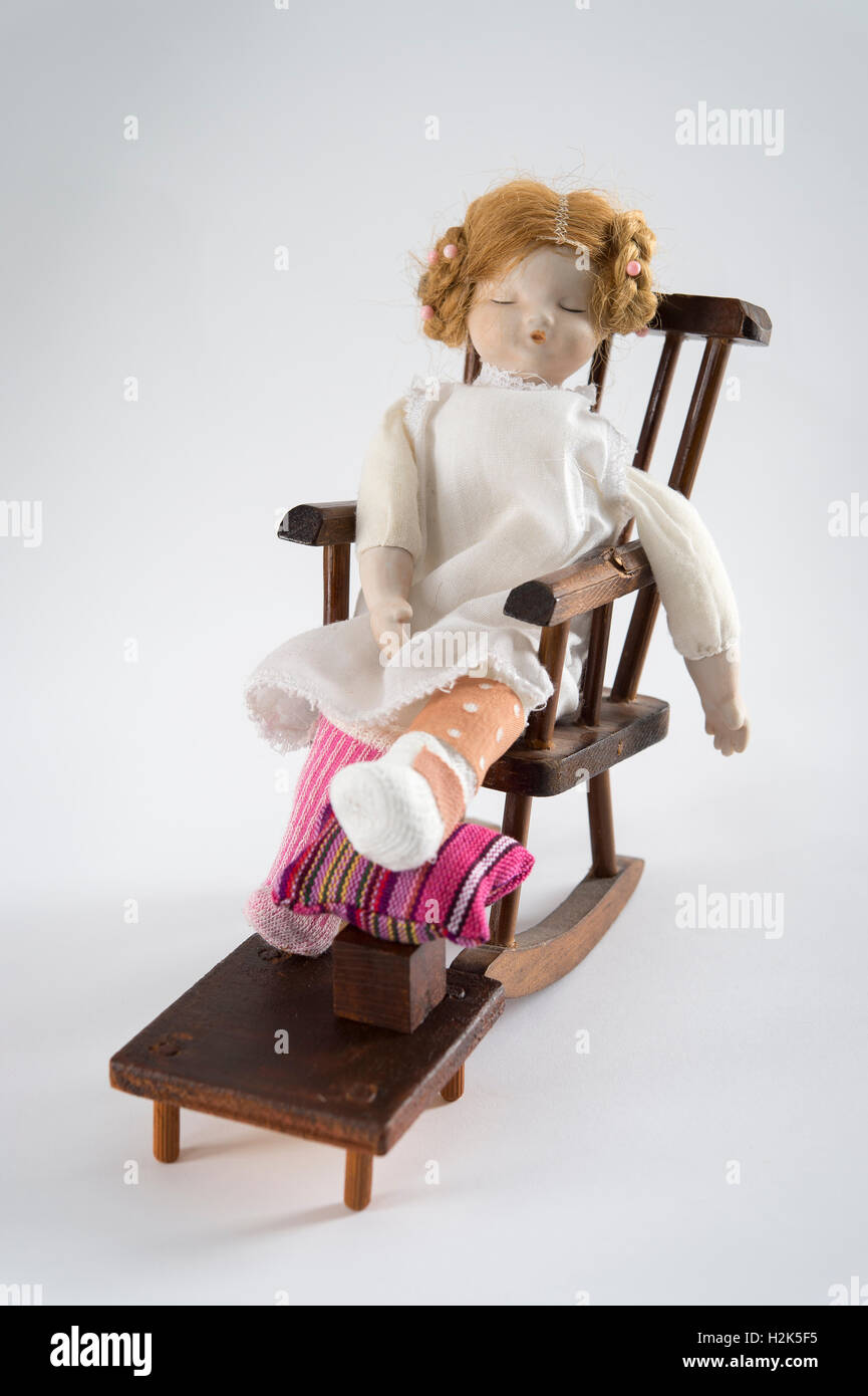 Doll endormi dans un fauteuil à bascule, la jambe bandée sur tabouret avec coussin, fond blanc Banque D'Images
