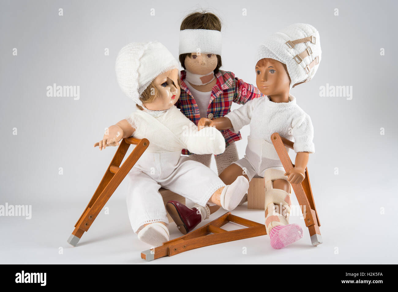 Trois poupées assis, des bandages sur la tête, la jambe d'une attelle, béquilles, eye patch, bras et l'épaule bandage, NECK BRACE, fond blanc Banque D'Images