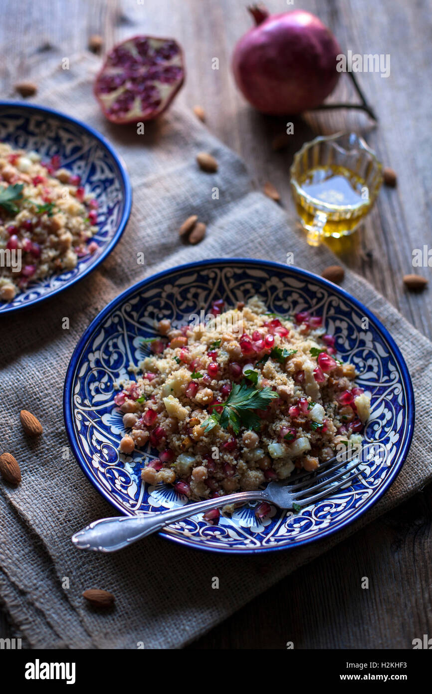 Couscous aux pois chiches, les amandes et la grenade sur les plaques en céramique bleu et table en bois rustique Banque D'Images