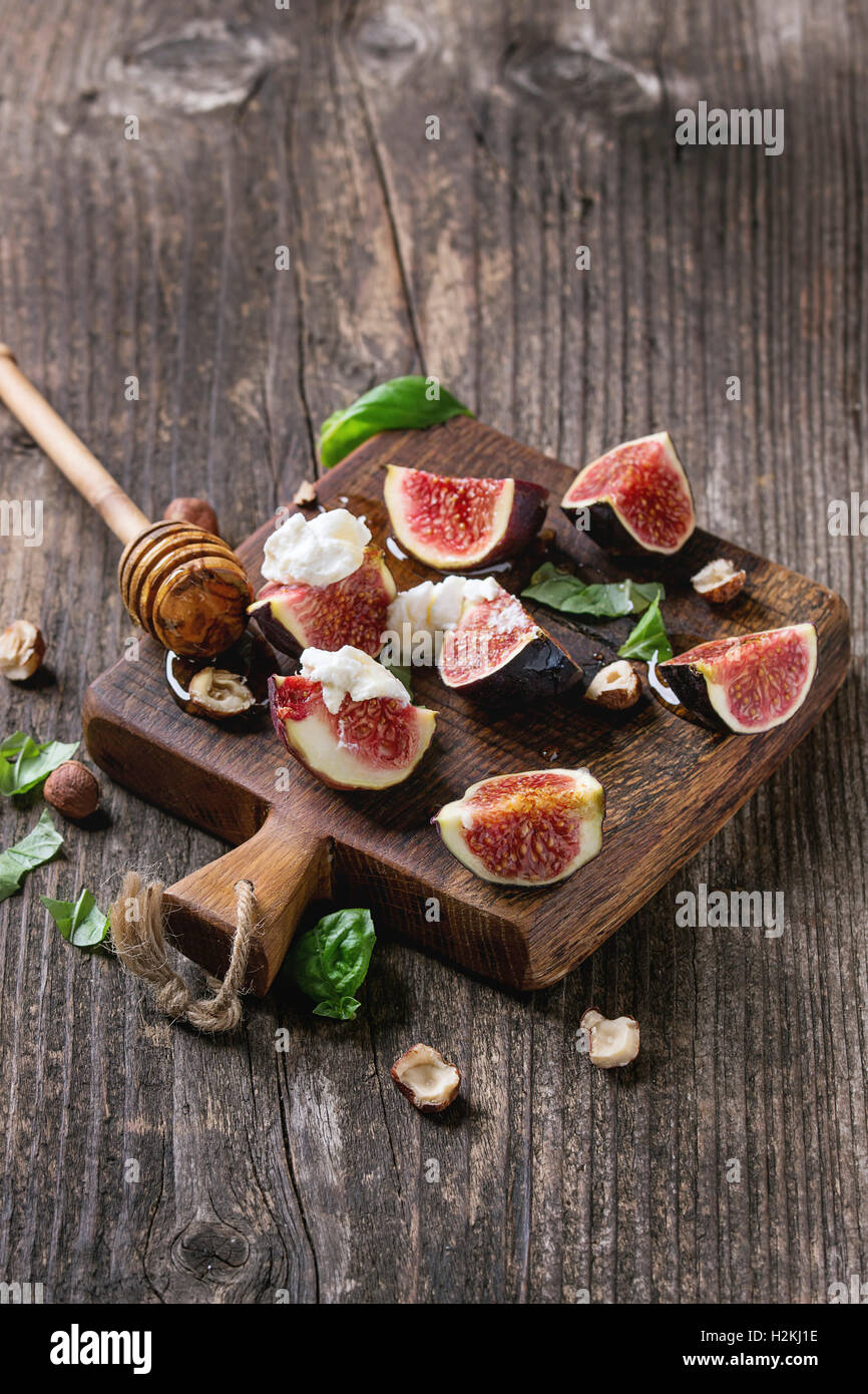 Figues fraîches tranches de fromage ricotta, de feuilles de basilic, de noisette et de miel miel de balancier sur petite planche à découper en bois foncé dessus Banque D'Images