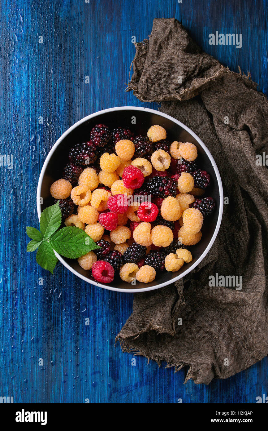 Bol de framboises rouges et jaunes aux couleurs vives et de Dewberry noir avec feuille de sacs chiffon sur fond texturé en bois bleu. Banque D'Images