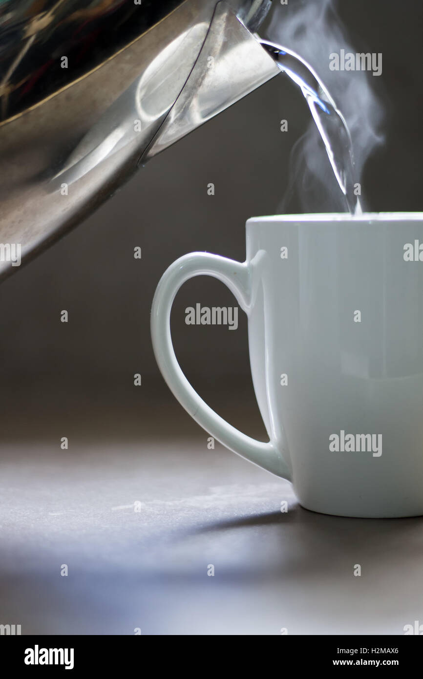 Verser de l'eau bouillante dans une tasse en céramique pour créer une boisson chaude. Banque D'Images