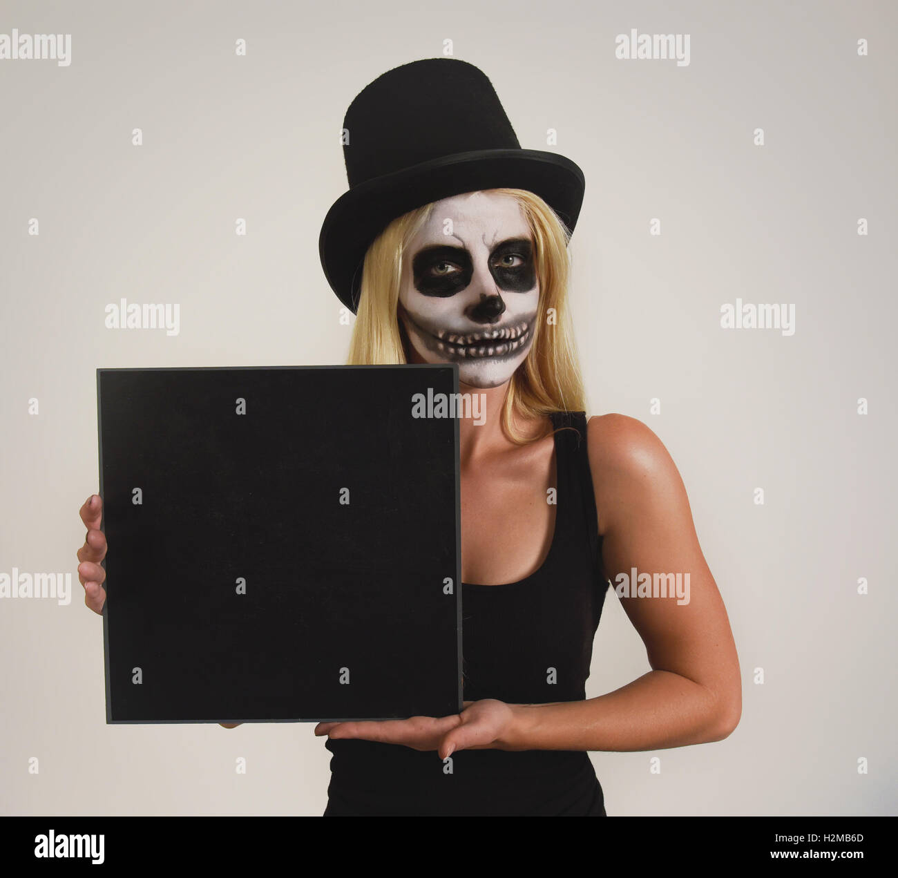 Une jeune fille porte un chapeau noir avec un squelette effrayant peinture maquillage sur son visage holding a blank sign pour un message d'halloween Banque D'Images