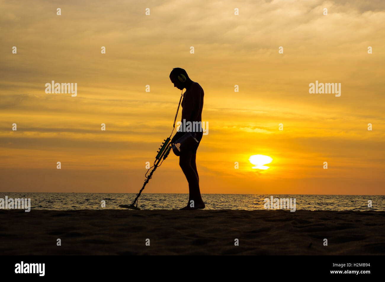 Un chasseur de trésor avec détecteur de métal sur le coucher du soleil sur la plage Banque D'Images
