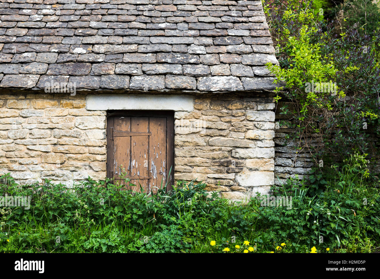 Ancien bâtiment en pierre avec petite porte en bois partiellement caché. Banque D'Images