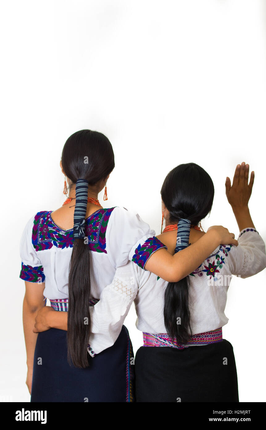 Belle hispanique mère et fille portant des vêtements traditionnelle des Andes, les embrassant tout en agitant, vus de derrière, l'angle fond studio blanc Banque D'Images