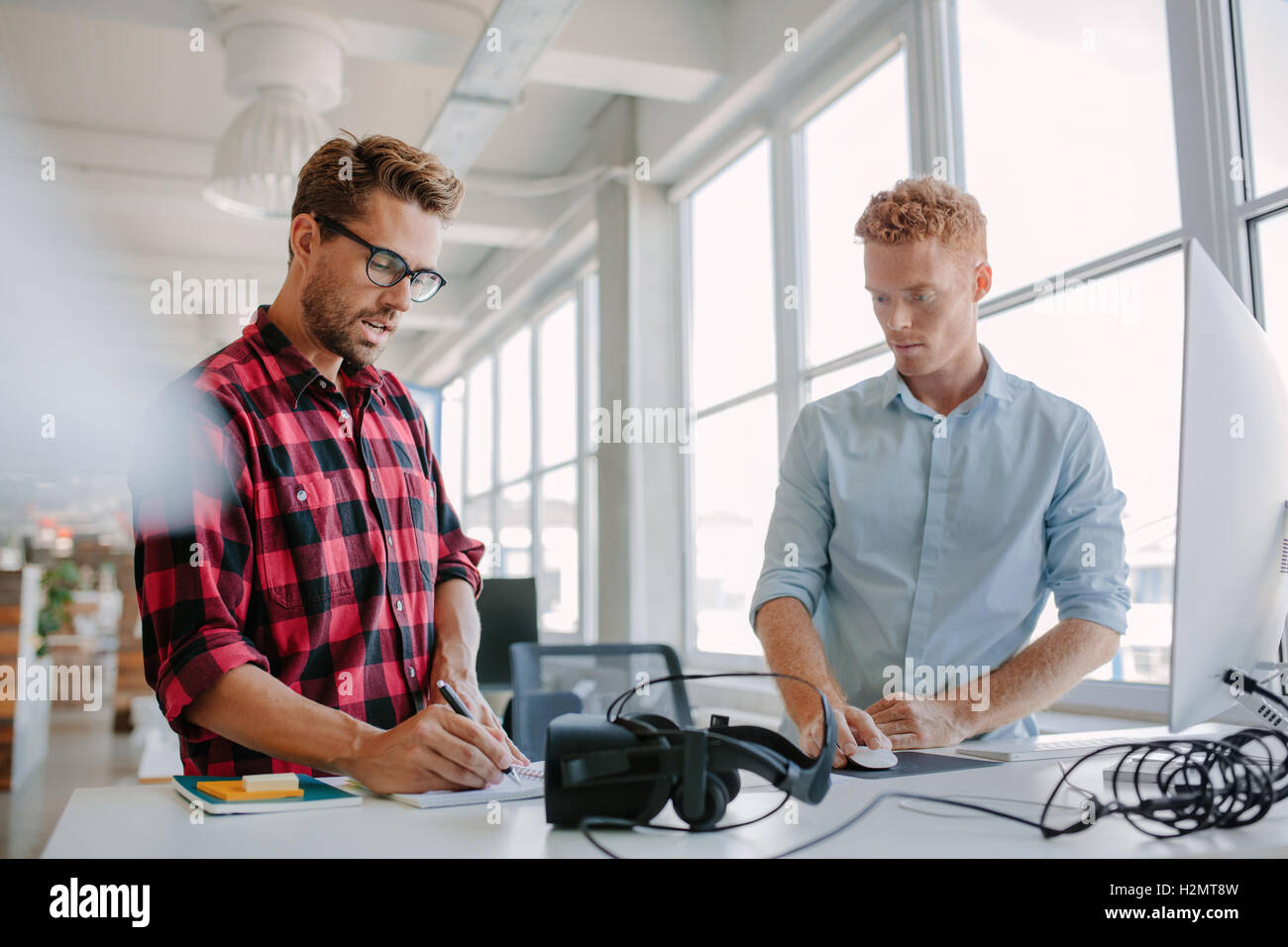 Deux jeunes businessman travaillant ensemble. Ils sont debout à une table avec des lunettes de réalité virtuelle. À l'aide d'un ordinateur et d'autres Banque D'Images