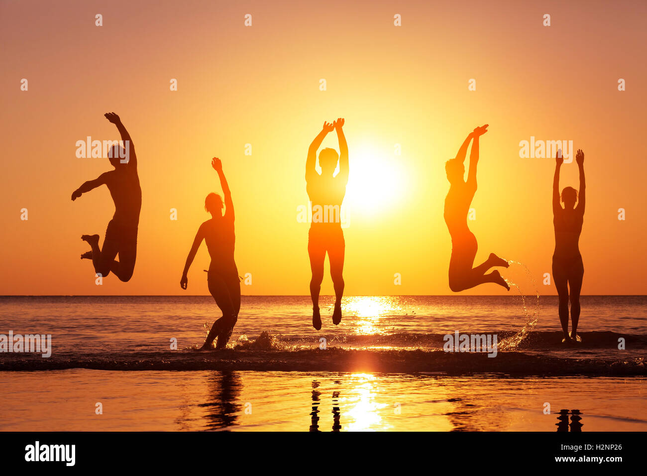 Groupe de gens heureux qui saute dans la mer au coucher du soleil, concept de s'amuser sur la plage, silhouette Banque D'Images