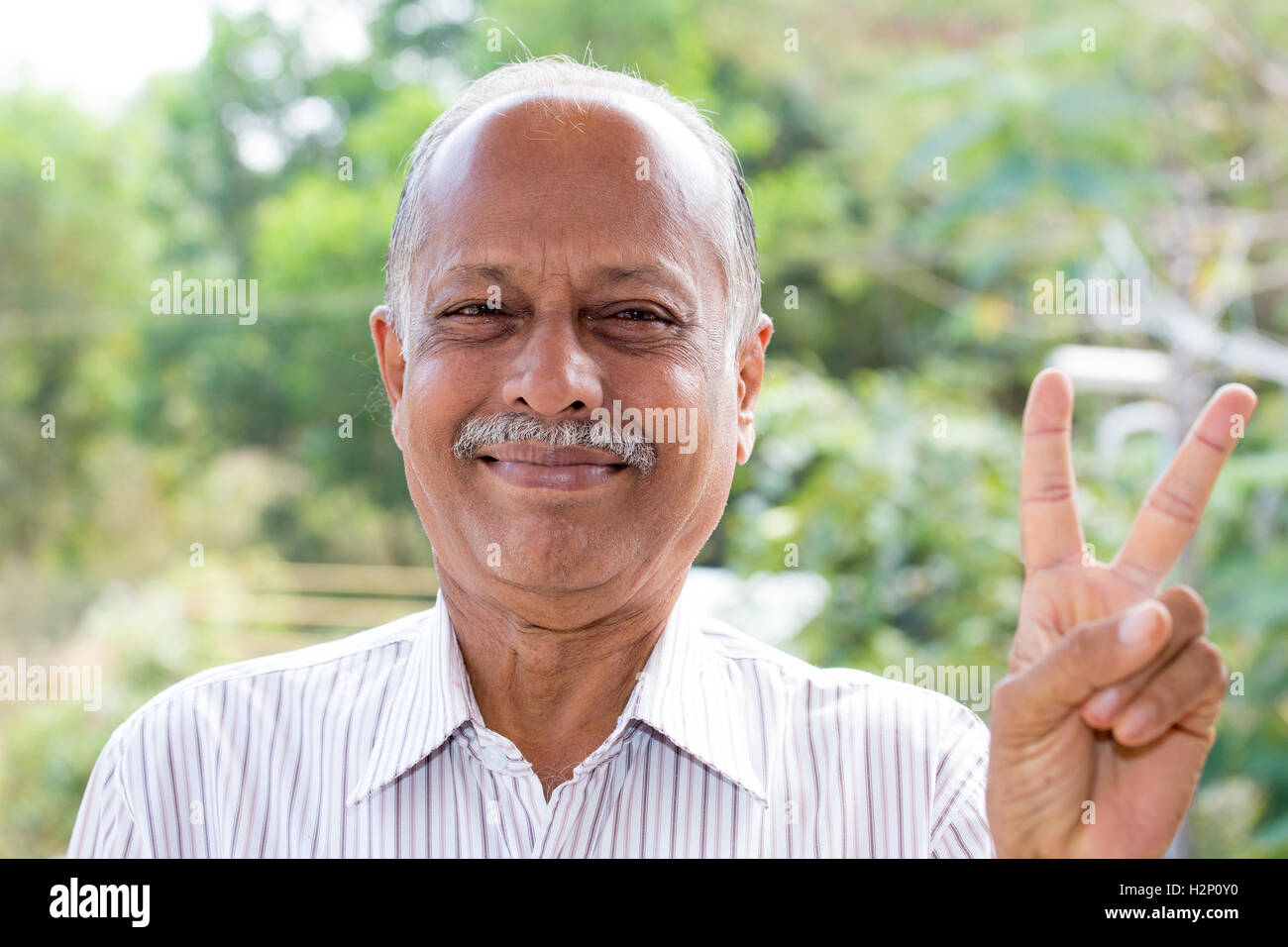 Closeup portrait, joyeux monsieur âgé en chemise rayée blanc holding up deux doigts, isolé à l'extérieur l'extérieur contexte Banque D'Images