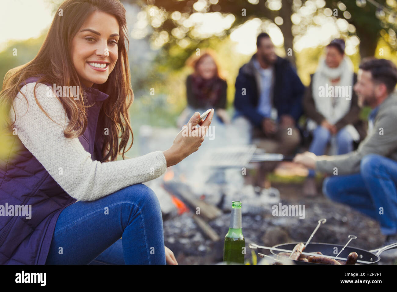 Portrait of smiling woman texting et boire de la bière au camping Banque D'Images