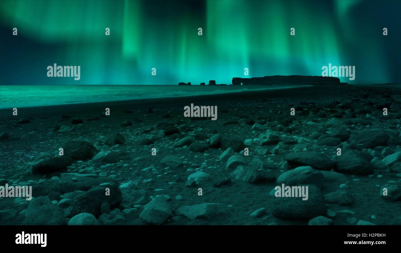 Photo composite montrant les aurores boréales vues de la plage de Vik en Islande. La plage de Vik, connu localement sous le nom de Reynishverfi, est célèbre pour son sable volcanique noir. Les aurores boréales sont causées par des particules provenant du Soleil - les électrons principalement, mais aussi des protons â€" passionnant ou rayonnements l'oxygène et l'azote dans l'atmosphère qu'ils coulent le long de nos lignes de champ magnétique de la planète. La lueur se produit lorsque les atomes se recombinent ou devenir de-excité. Banque D'Images