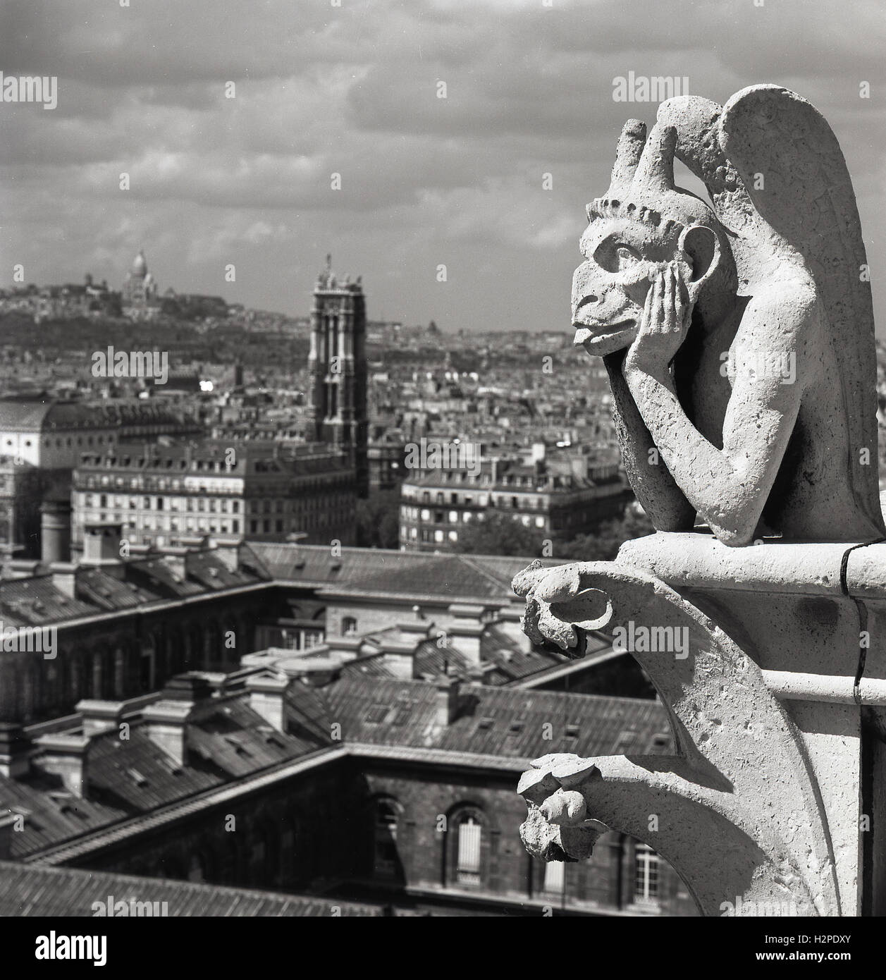 Années 1950, histoire, une chimère sur la cathédrale notre-Dame au-dessus de la ville de Paris, France. Contrairement aux célèbres gargouilles de notre-Dame, ces sculptures en pierre calcaire grotesques conçues comme des becs pour transporter l'eau de pluie loin du toit, ne dépassent pas des murs extérieurs. Au lieu de cela, ils bordent la Galerie des Chimères, un balcon qui relie les deux clochers. En se regardant au-dessus de la balustrade, où ils gardent le contrôle de la ville ci-dessous, ils ont été un nouvel ajout à la cathédrale au milieu des années 1800 lorsqu'elle a subi la restauration. 56 chimères ou grotesques comme ils sont connus ont été érigés. Banque D'Images