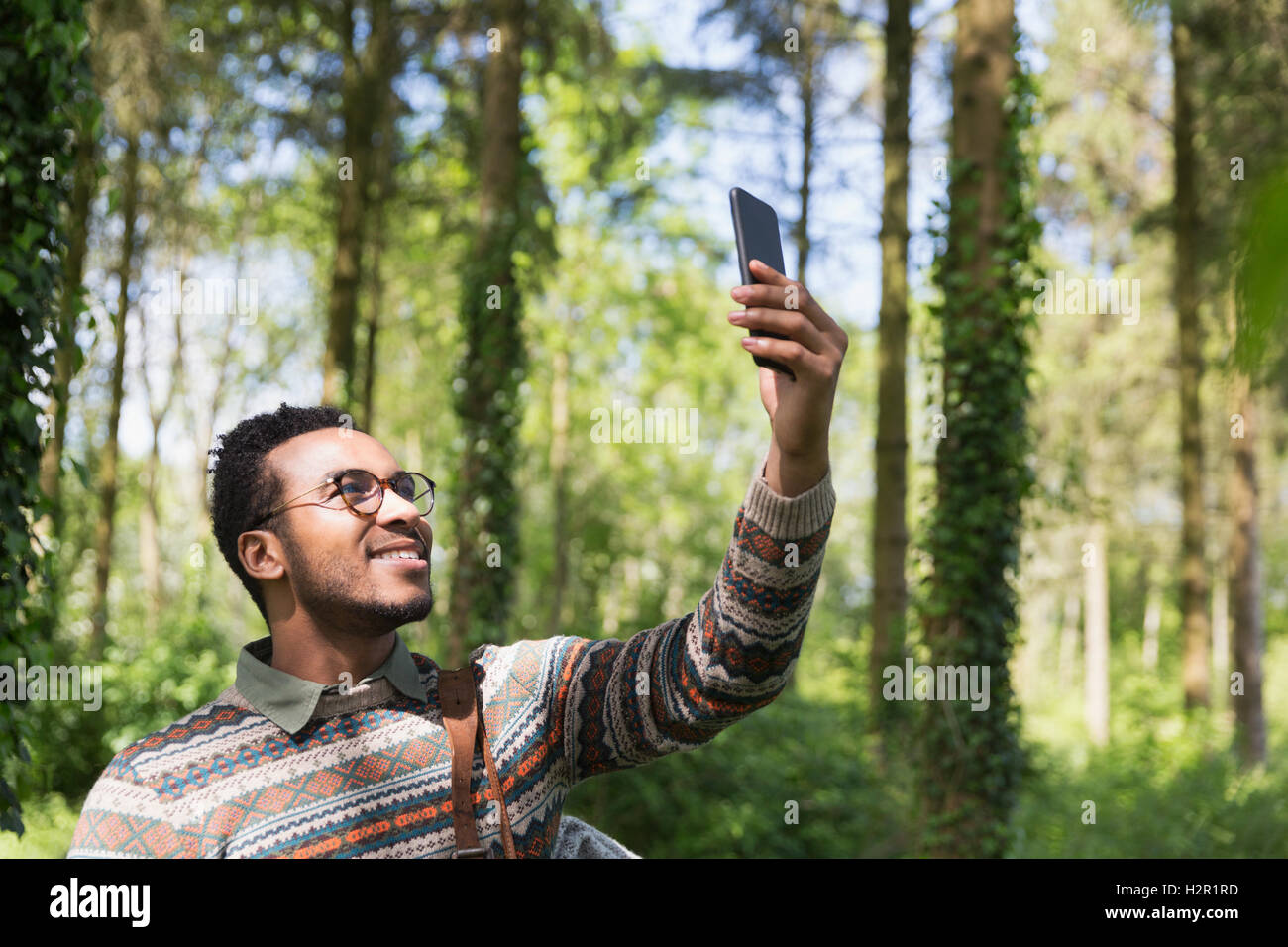 L'homme souriant en tenant avec selfies camera phone in sunny woods Banque D'Images