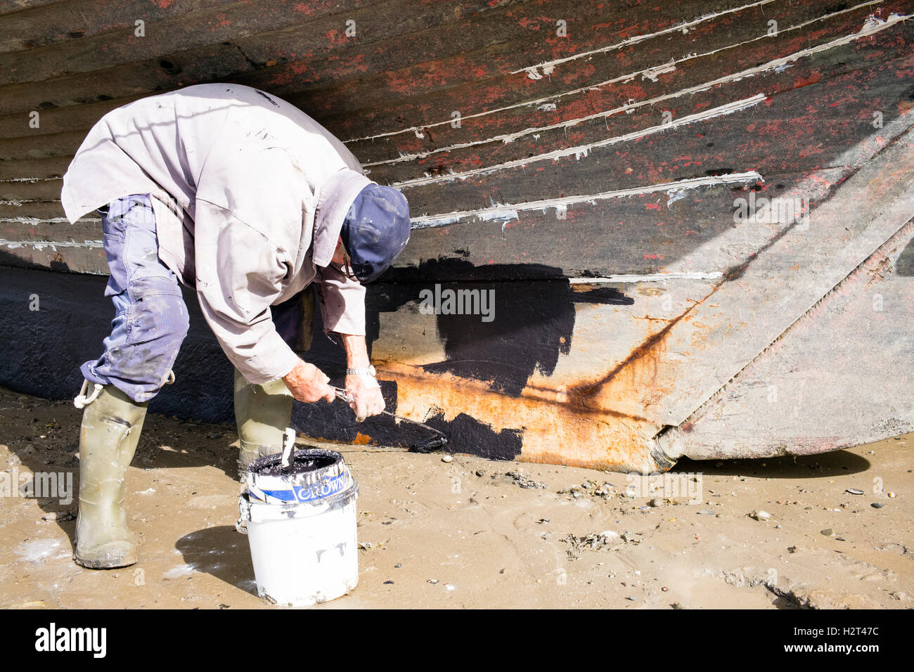 Un "vieux-sel' l'application de peinture antisalissure à la quille de son yacht, plage de Conwy, Pays de Galles, Royaume-Uni Banque D'Images