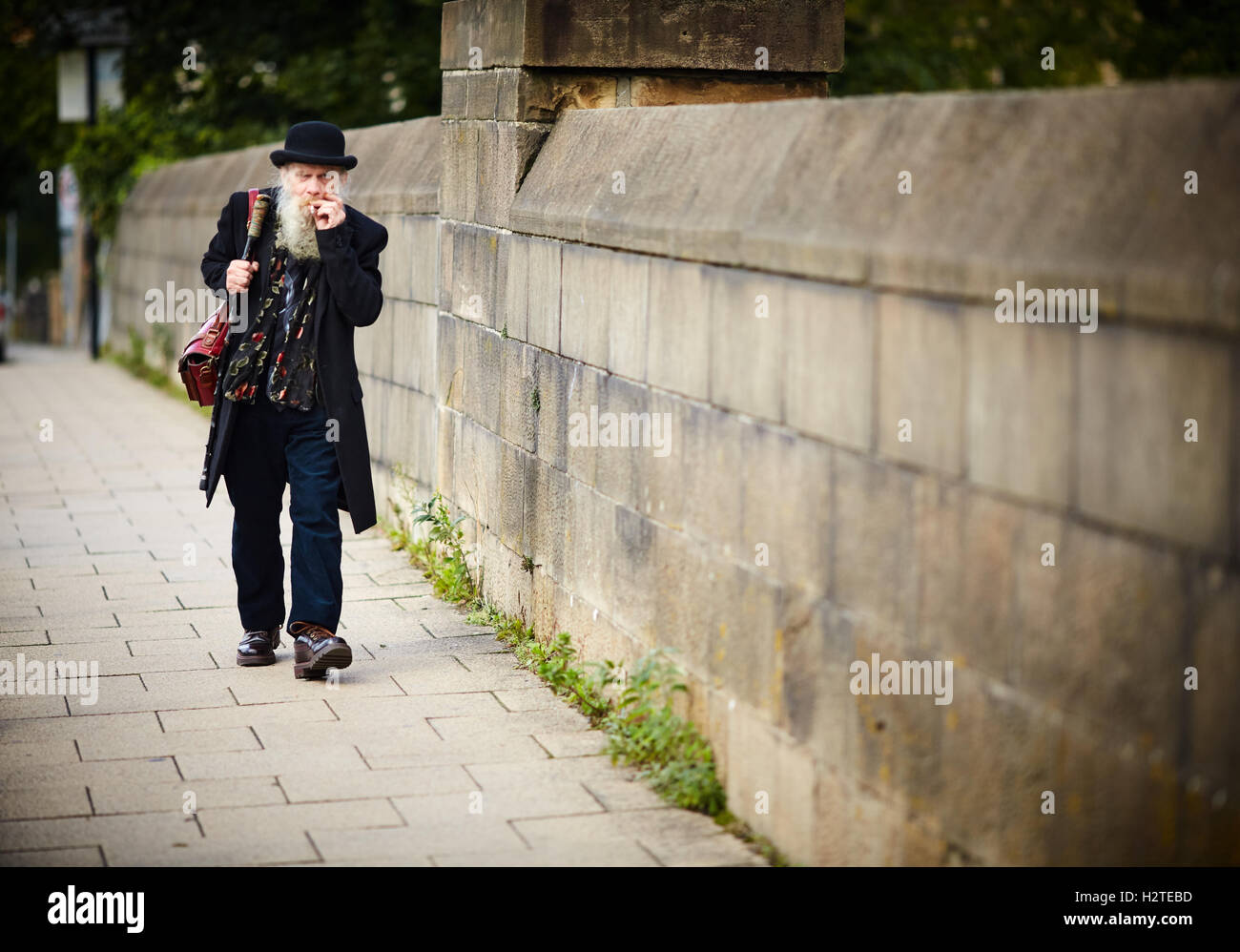 Caricature caricature Lancaster vieil homme avec chapeau melon marcher sur un pont dans le centre-ville, noir foncé de l'habillement et du cuir style hobo sac Banque D'Images