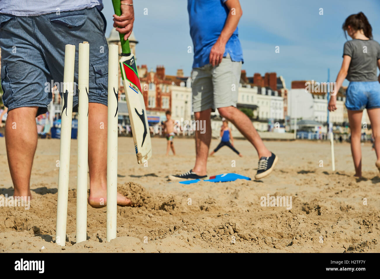 Famille et amis profitant d'une partie de cricket de plage sur une plage de sable. Banque D'Images