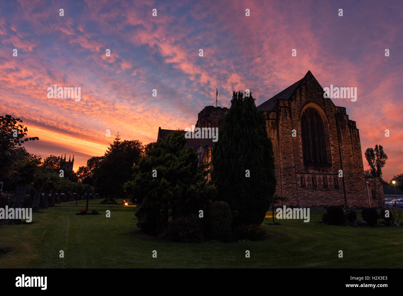 Magnifique coucher de soleil sur serein une église, avec le rose et orange nuages dans un ciel bleu parfait, entouré d'arbres et d'herbe. Banque D'Images