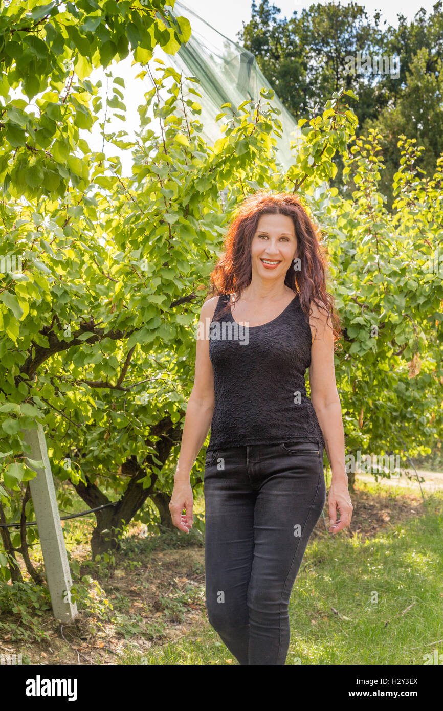Rouge nice woman enjoying nature d'une campagne tout en marchant dans le verger en saison d'automne Banque D'Images