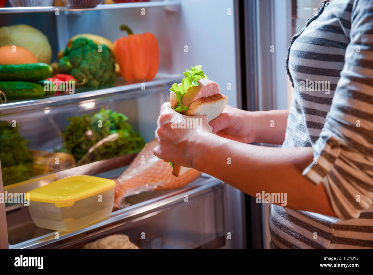 Hungry Woman holding un sandwich dans ses mains et se tenait à côté de l'Open d''un réfrigérateur. Aliments malsains. Banque D'Images