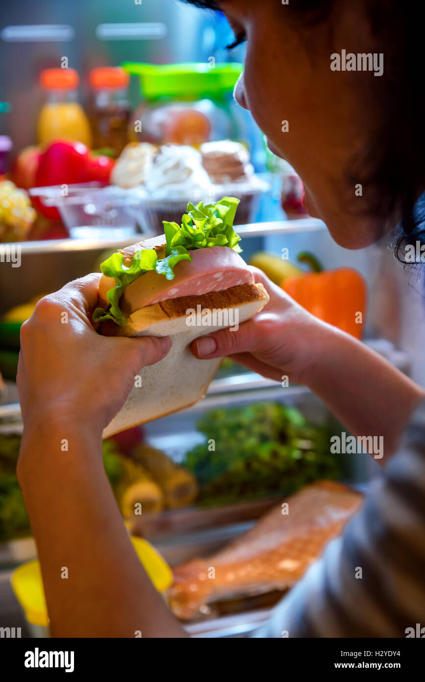 Hungry Woman holding un sandwich dans ses mains et se tenait à côté de l'Open d''un réfrigérateur. Aliments malsains. Banque D'Images