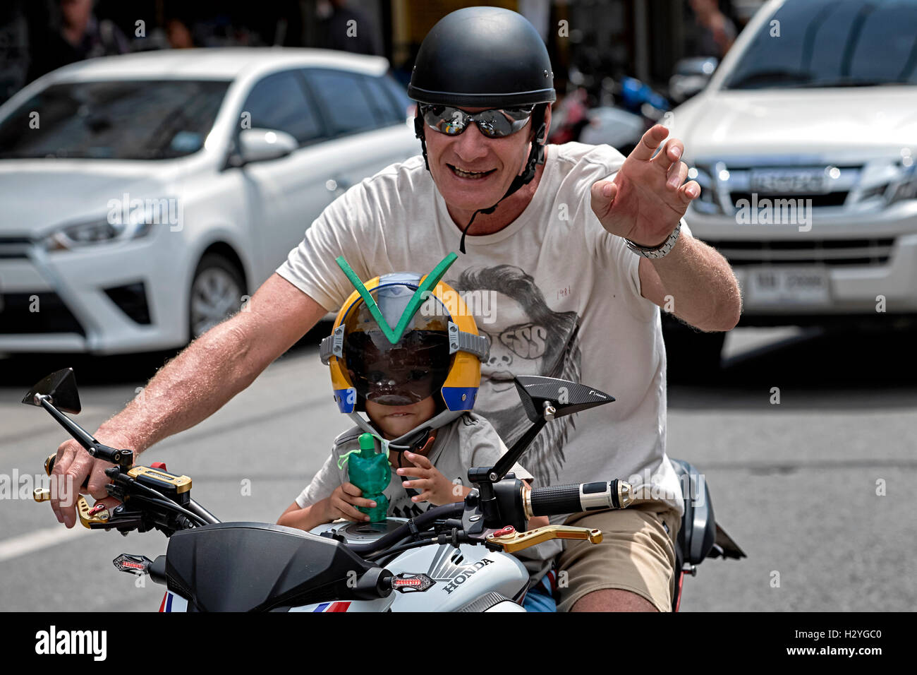 Moto enfant. Père transportant son jeune enfant sur une moto à travers la circulation. Banque D'Images