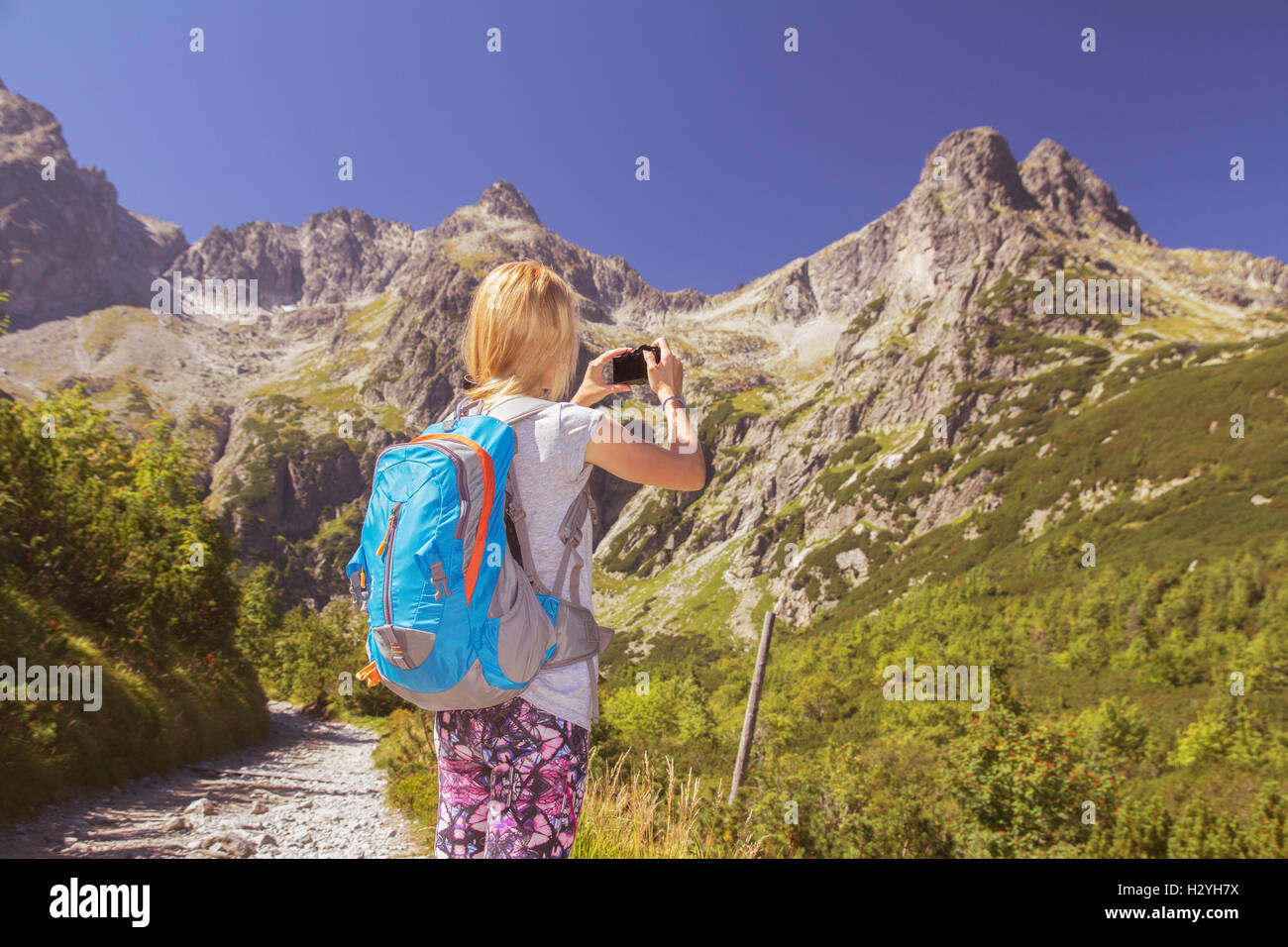 Jeune femme backpacker de prendre des photographies d'une montagne alpine pittoresque comme elle se tient dans le soleil de l'été sur un sentier ou tra Banque D'Images