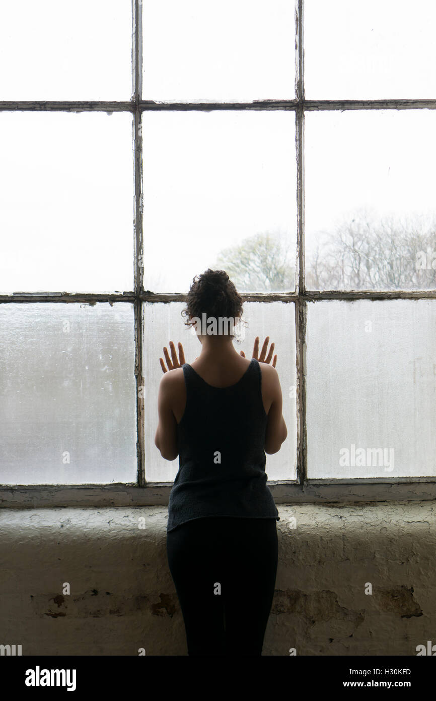 Vue arrière d'une jeune femme debout près de la fenêtre les mains de toucher le verre Banque D'Images