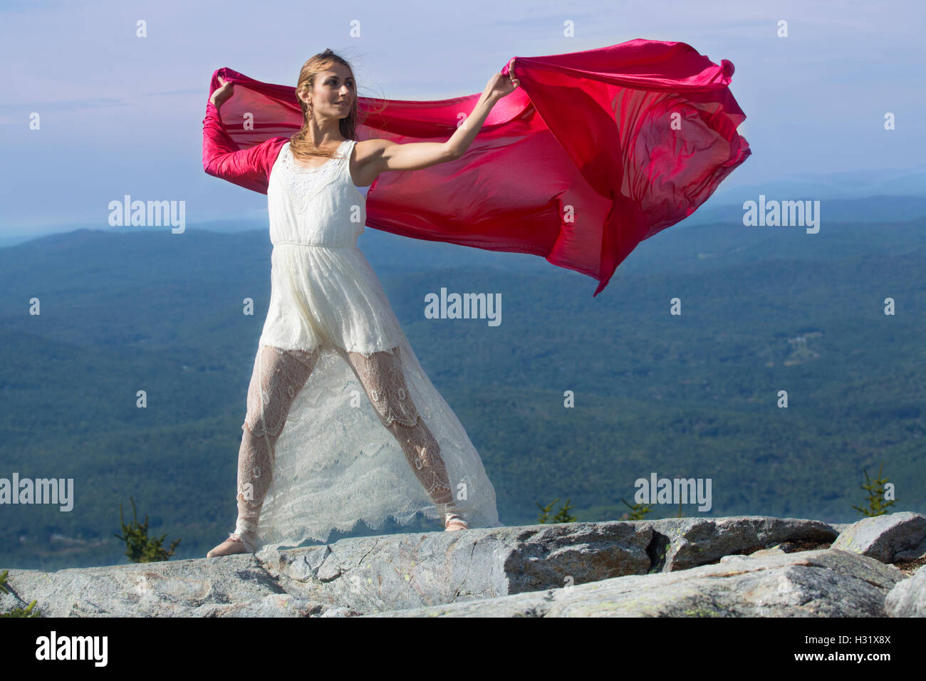Danseuse en robe blanche tissu rouge ondulant dans le vent au sommet de Mt. Kearsarge, NH. Banque D'Images