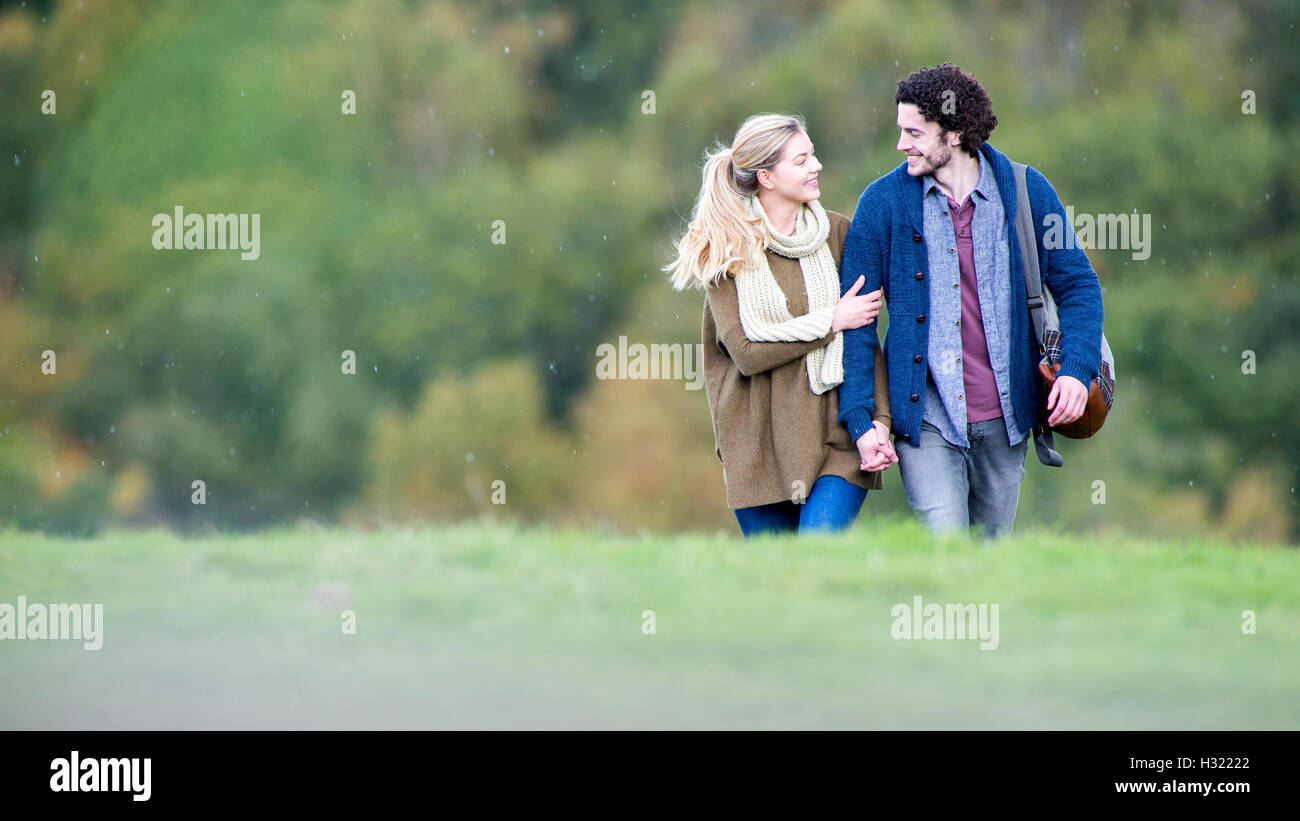 Jeune couple en train de marcher ensemble sur un jour de pluie. Ils sont tenant la main et de parler. Banque D'Images