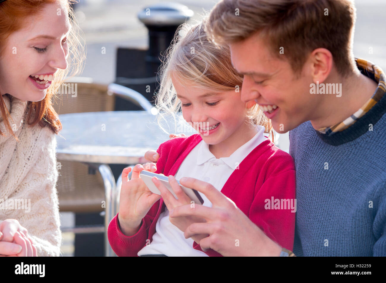 Jeune couple à la recherche de quelque chose de drôle sur un smartphone avec leur fille. Elle est wearig son uniforme scolaire. Banque D'Images