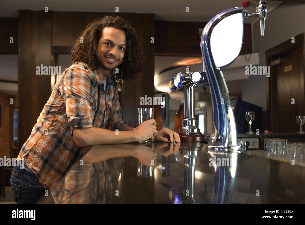 Jeune homme debout dans un bar avec une pinte, souriant à la caméra. Banque D'Images
