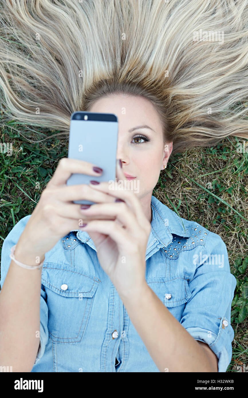 Belle jeune blonde allongée sur l'herbe et prendre des selfies Banque D'Images