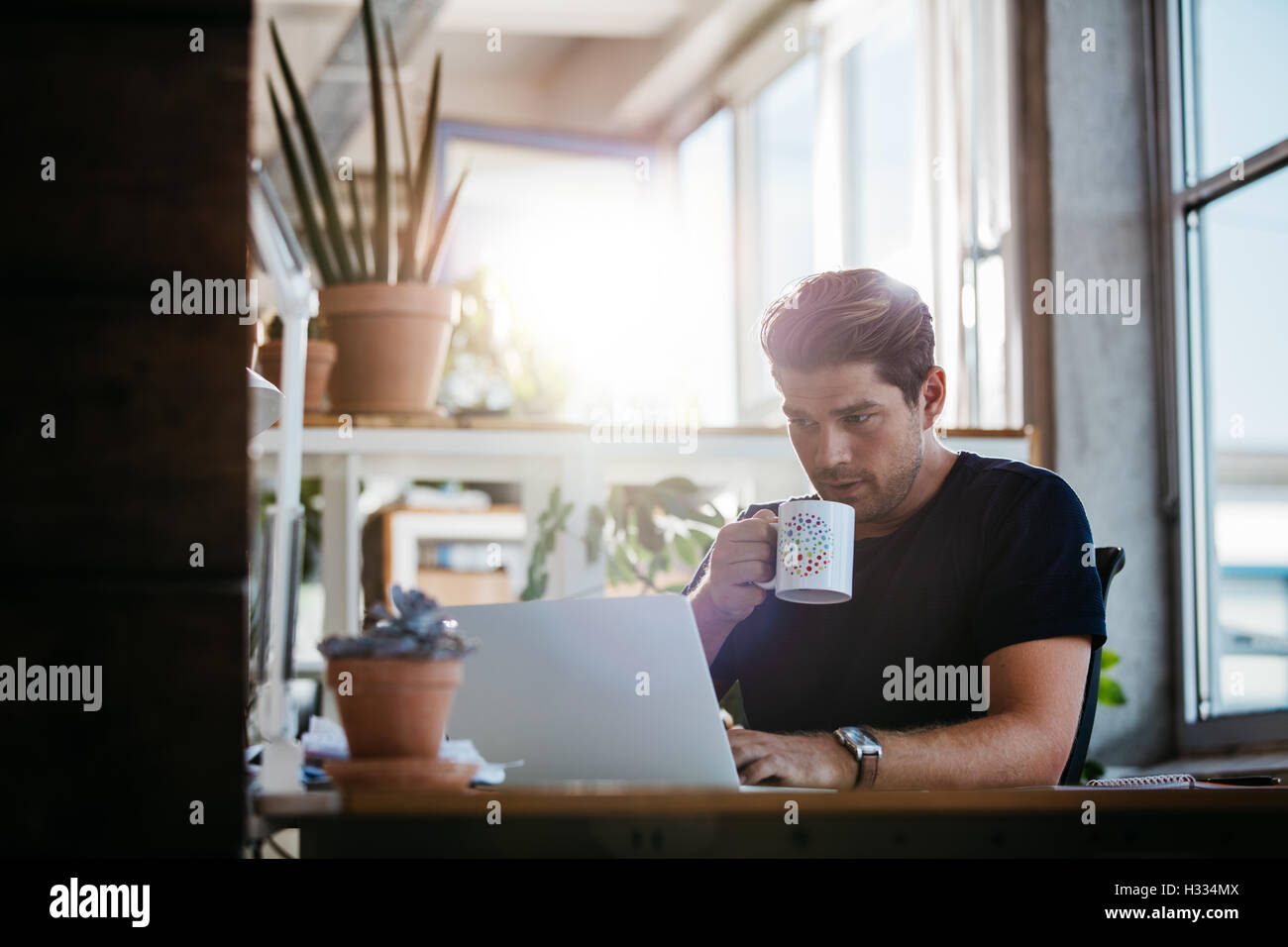 Jeune homme d'affaires assis à son bureau travaillant sur les ordinateurs portables et de boire du café. Jeune homme de travail moderne surf internet. Banque D'Images