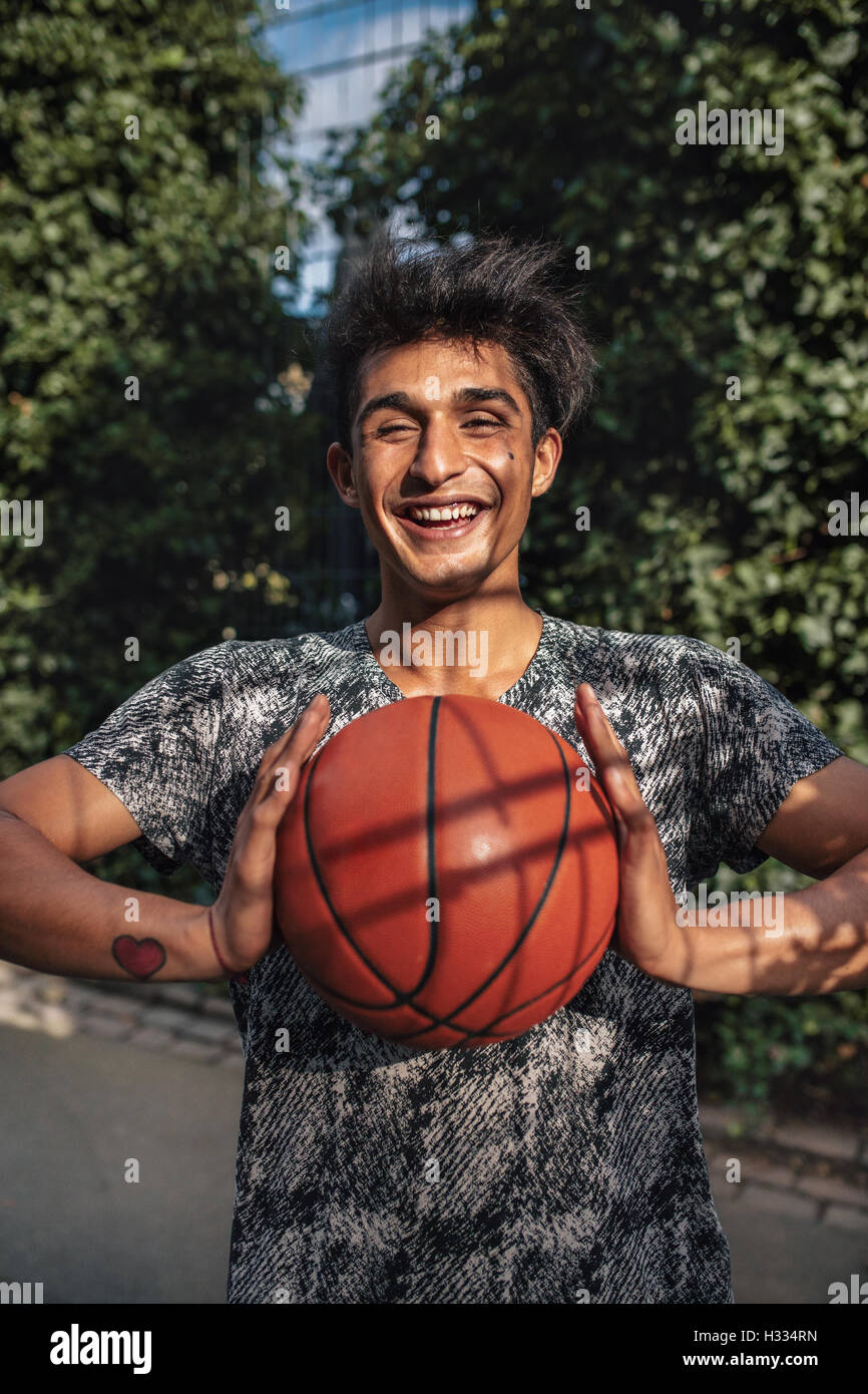 Portrait of smiling young man passant au basket-ball. Teenage guy looking at camera avec un ballon dans les mains sur la cour extérieure. Banque D'Images