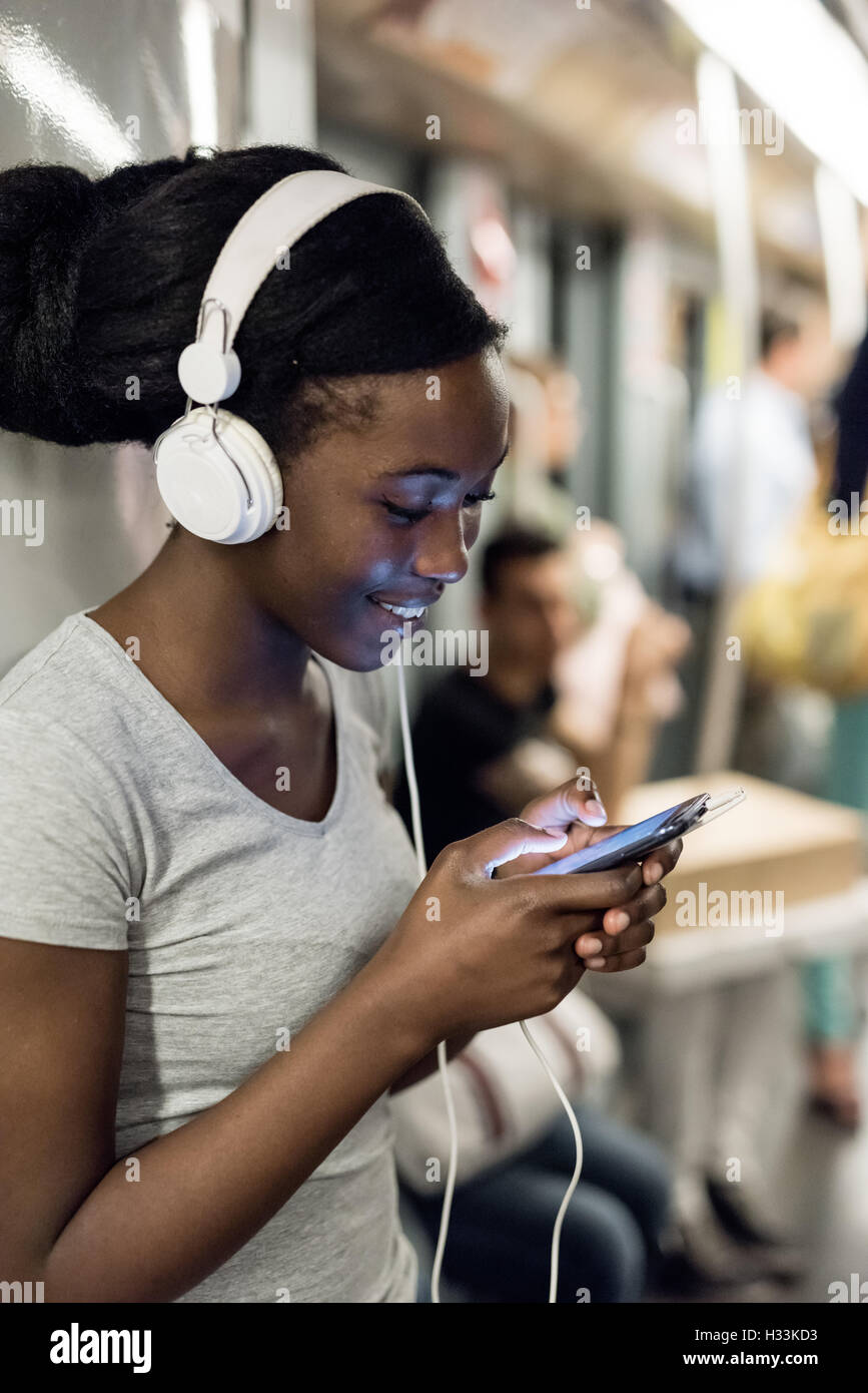 Jeune femme noire à l'écoute de la musique avec des écouteurs et l'aide de smart phone part tenir voyageant dans le métro, smiling - commut Banque D'Images