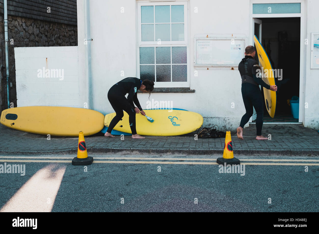 Nettoyage surfeur jaune sable au large de planches de surf après une leçon à Sennen Cove Recreation Centre, Cornwall Banque D'Images