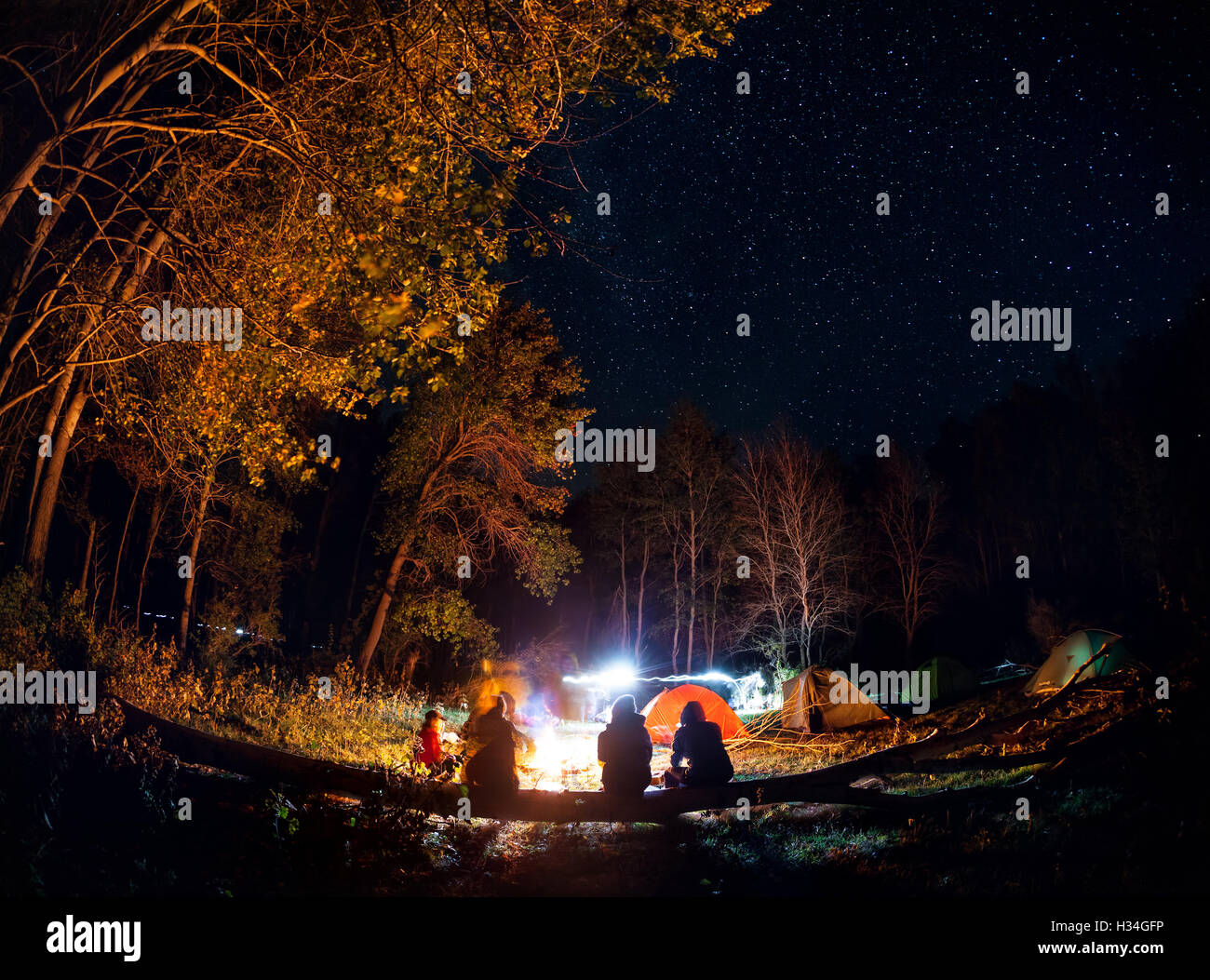 Les gens au camp touristique en forêt avec feu à tente autour de la nuit ciel étoilé Banque D'Images