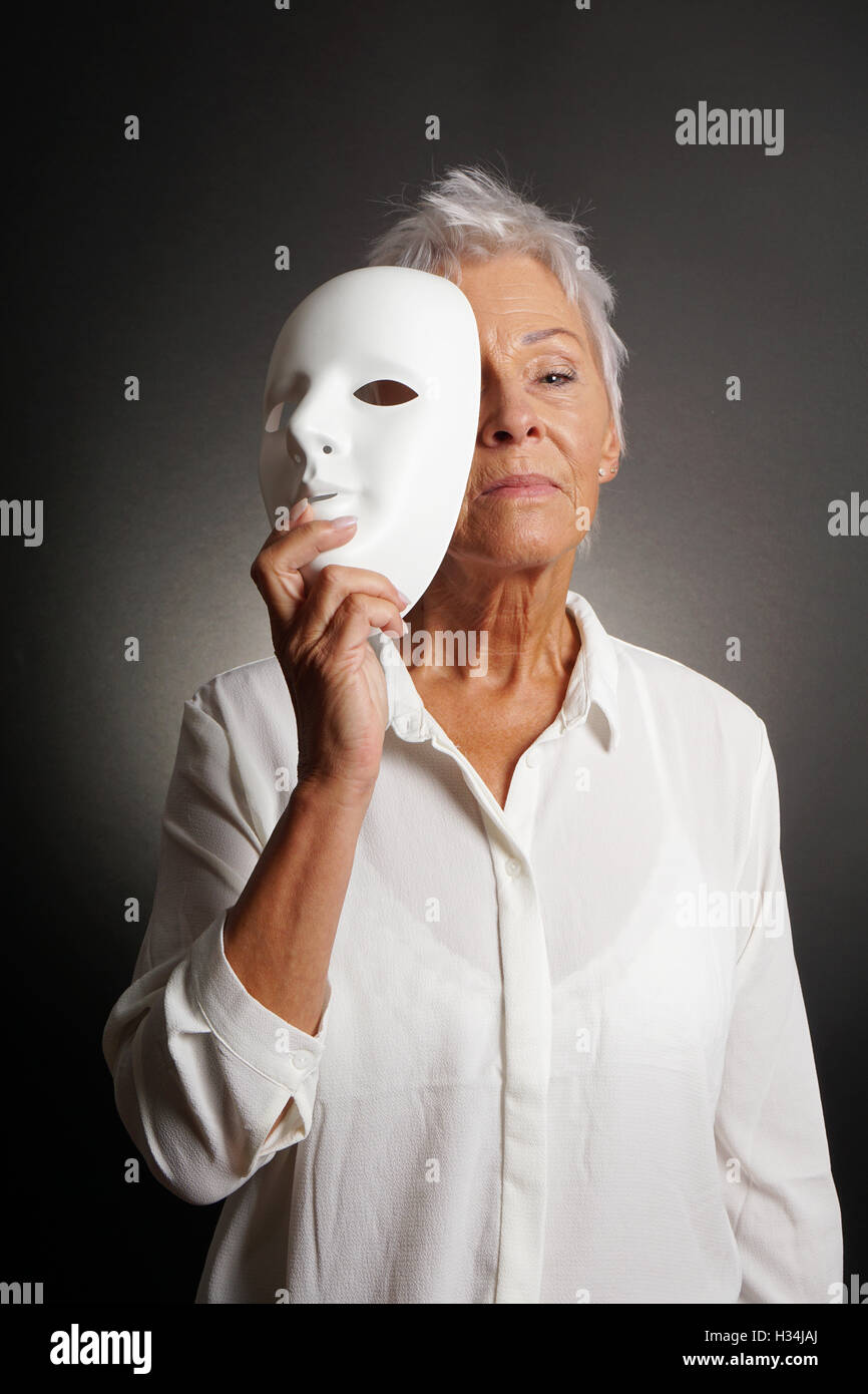 Femme mature sérieux révélant derrière face mask Banque D'Images