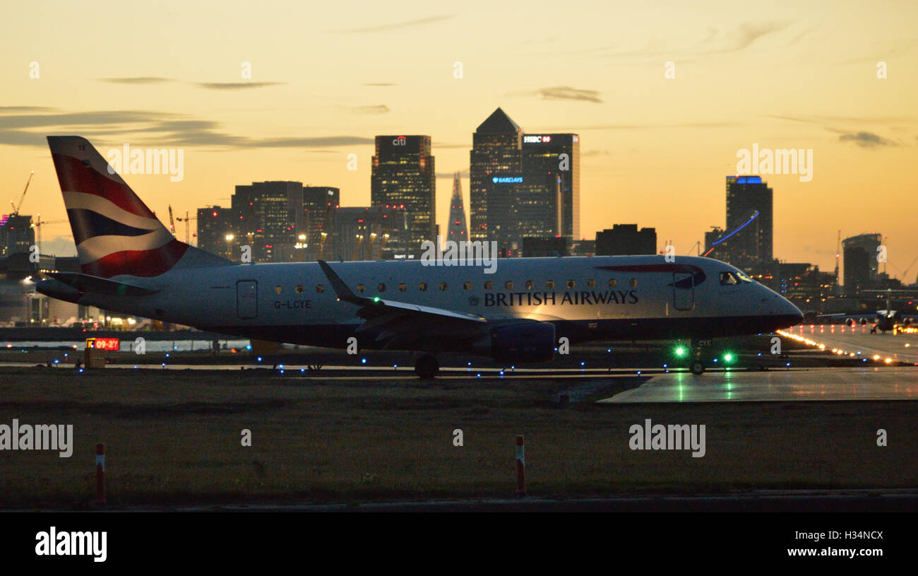 BA CityFlyer Embraer 170 la queue pour décoller de l'aéroport de London City que le soleil se couche derrière les toits de Londres Banque D'Images